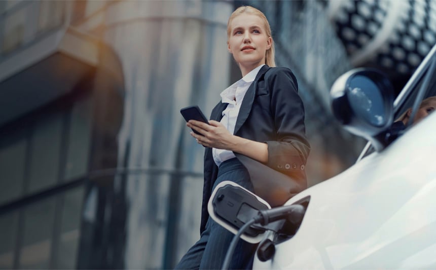 Geschäftsfrau lehnt entspannt an einem Elektroauto mit Ladekabel vor modernem Bürogebäude – Sinnbild für E-Mobilität und Innovation.