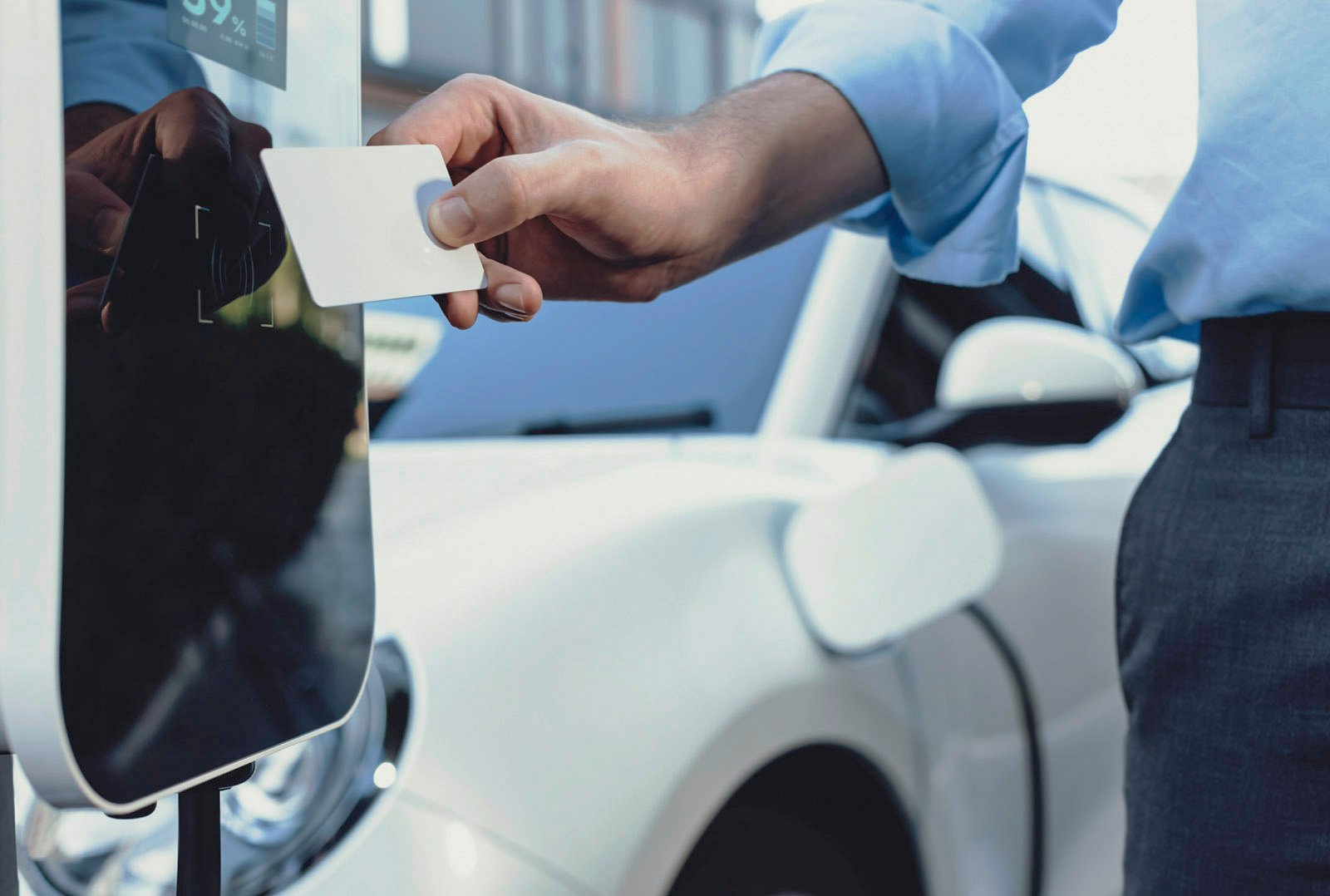 Mann hält RFID-Karte vor Ladesäule zum Starten des Ladevorgangs eines weißen Elektroautos – Symbol für moderne Ladeinfrastruktur am Unternehmensstandort