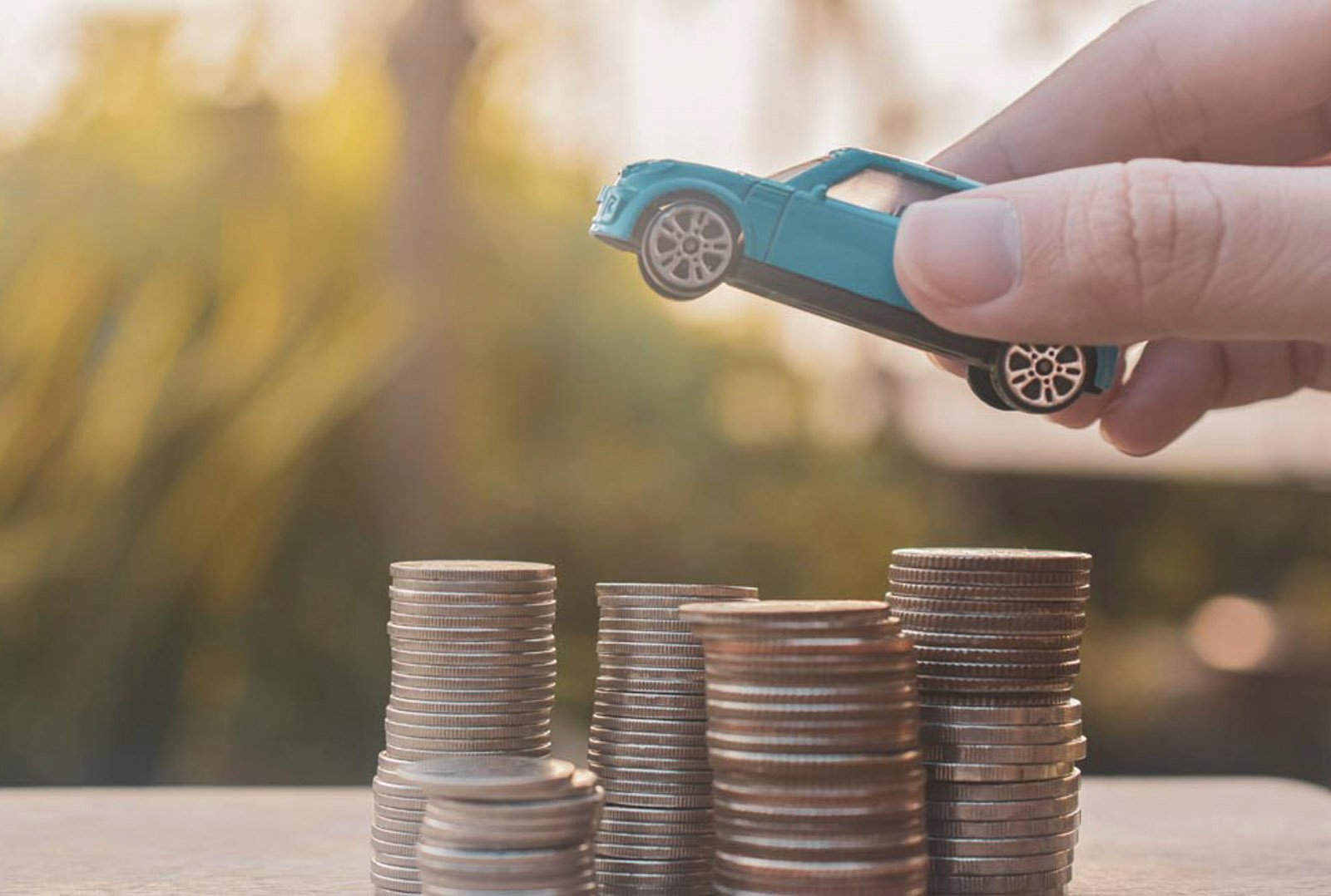 Hand setzt Spielzeugauto auf gestapelte Münzen – Symbol für THG-Prämie und finanzielle Vorteile